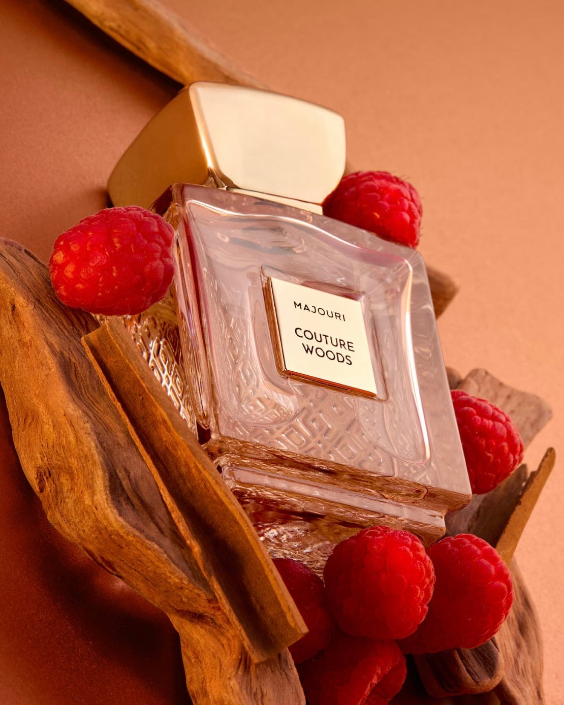 Majouri Couture Woods parfumflacon met gouden dop, omringd door frambozen en stukken hout.